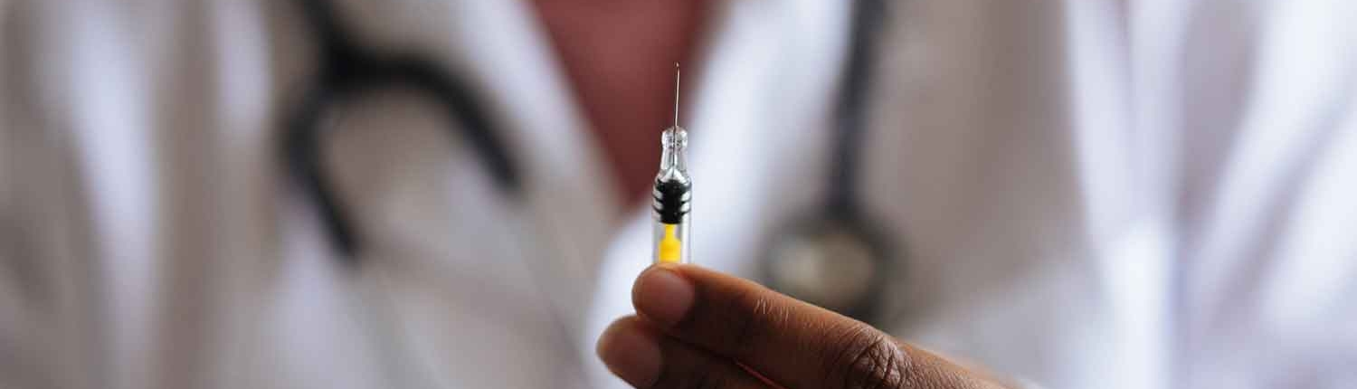 Close shot of a syringe held carefully between a young doctor's fingertips.