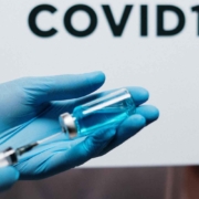 Close shot of a vaccine being drawn from a vial into a syringe. The word COVID-19 floats in the background.