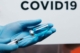 Close shot of a vaccine being drawn from a vial into a syringe. The word COVID-19 floats in the background.